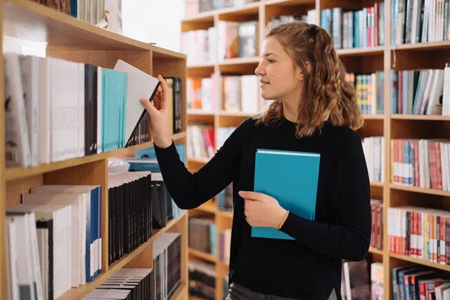 About us - teenager-girl-picking-book-library-shelf